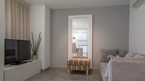 A modern living room with a flat-screen TV, a small stool, a grey sofa, and a white coffee table. - Malaga Apartments Andes (Málaga)
