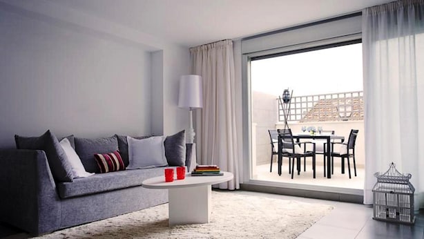 A modern living room with a grey sofa, a white coffee table, and a view of an outdoor balcony with a dining area. - Malaga Apartments Andes (Málaga)