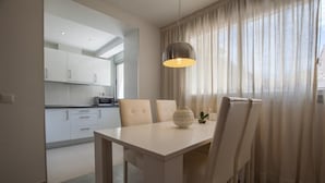 A dining area with a white table and chairs, a hanging pendant light, and a view of a kitchen in the background. - Malaga Apartments Andes (Málaga)