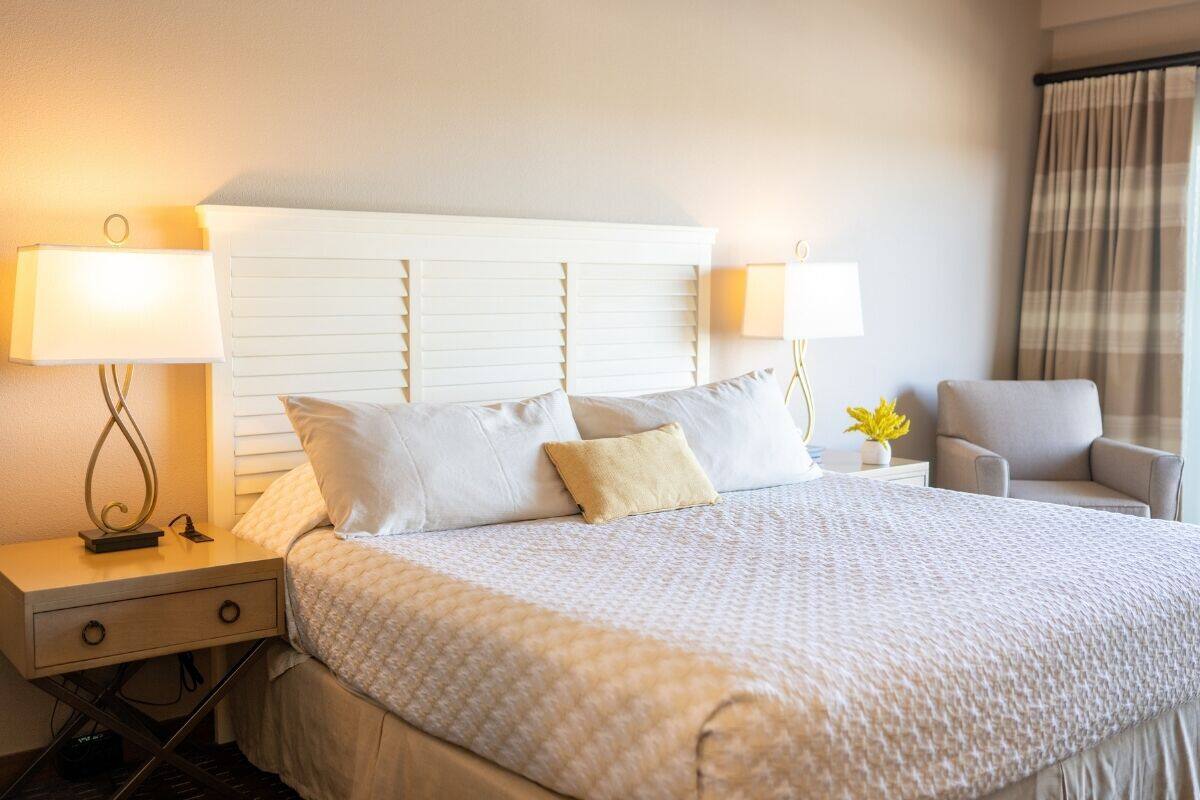 Habitación de hotel con una cama grande, dos lámparas de noche, una silla y una mesita de noche con lámpara.