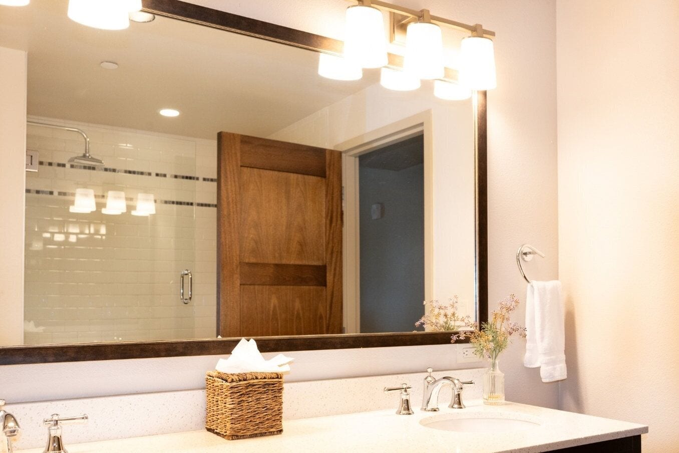 A bathroom with a large mirror, a wooden door, a sink, and a towel rack.