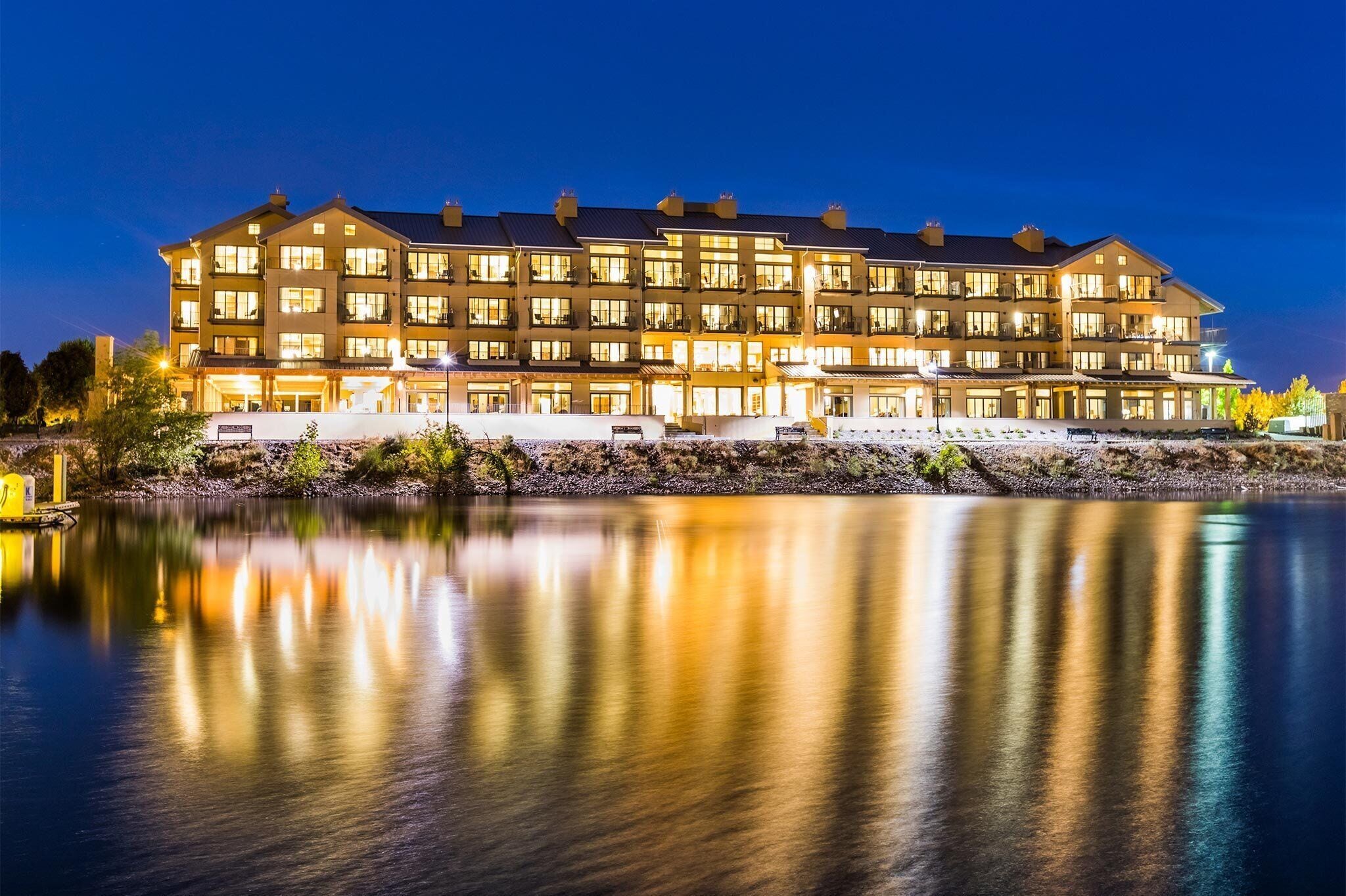 A multi-story hotel with a reflective pool in front, featuring a well-lit facade and a waterfront view.