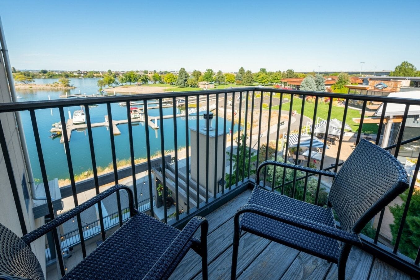 A balcony with two wicker chairs, overlooking a marina with boats and a swimming pool.