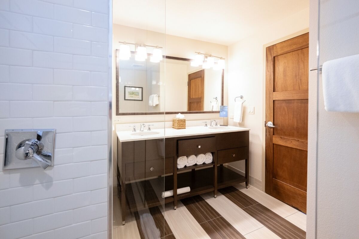 A bathroom with a double sink, a large mirror, a wooden door, and a towel rack.