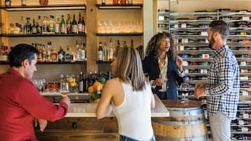 A bar area with shelves of bottles and glasses, a wooden barrel, and a wine rack in the background.
