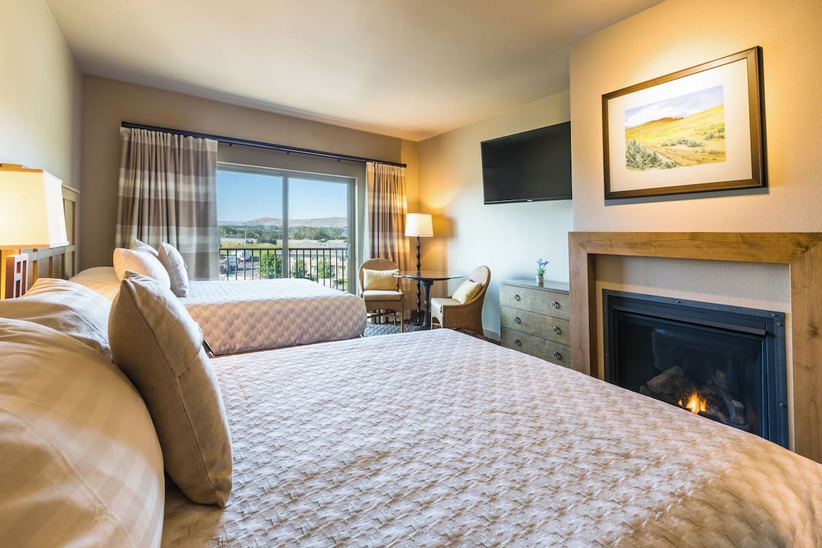 Habitación de hotel con una cama grande, chimenea, televisor montado en la pared y balcón con cortinas.