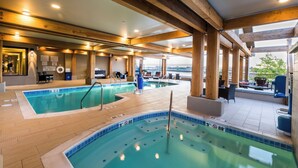 Un área de piscina interior con varias piscinas, vigas de madera y zonas de estar.
