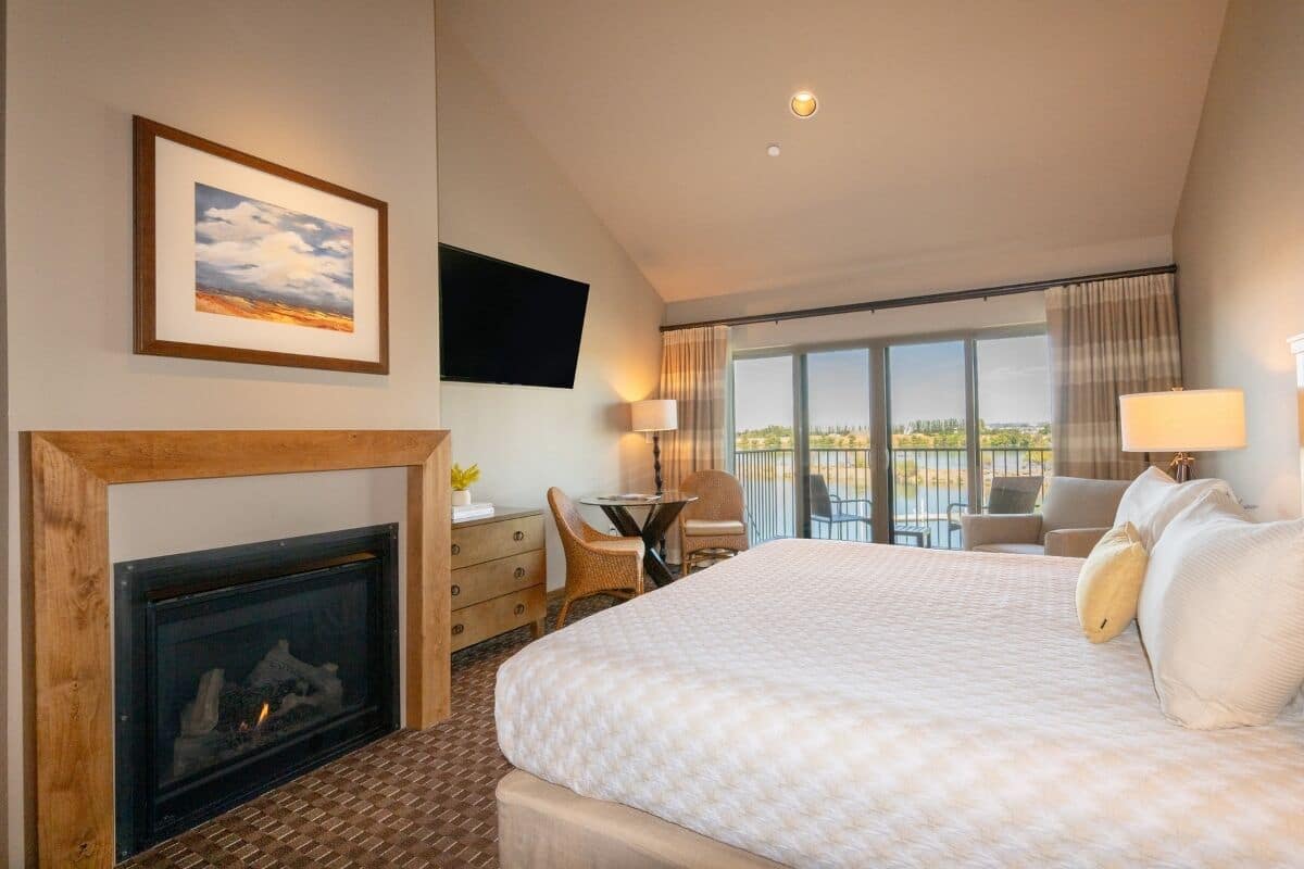 Habitación de hotel con una cama grande, chimenea, balcón con vistas y televisor de pantalla plana montado en la pared.