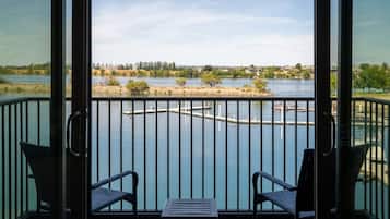 A balcony with two chairs and a small table, overlooking a calm lake with a dock and distant shoreline.