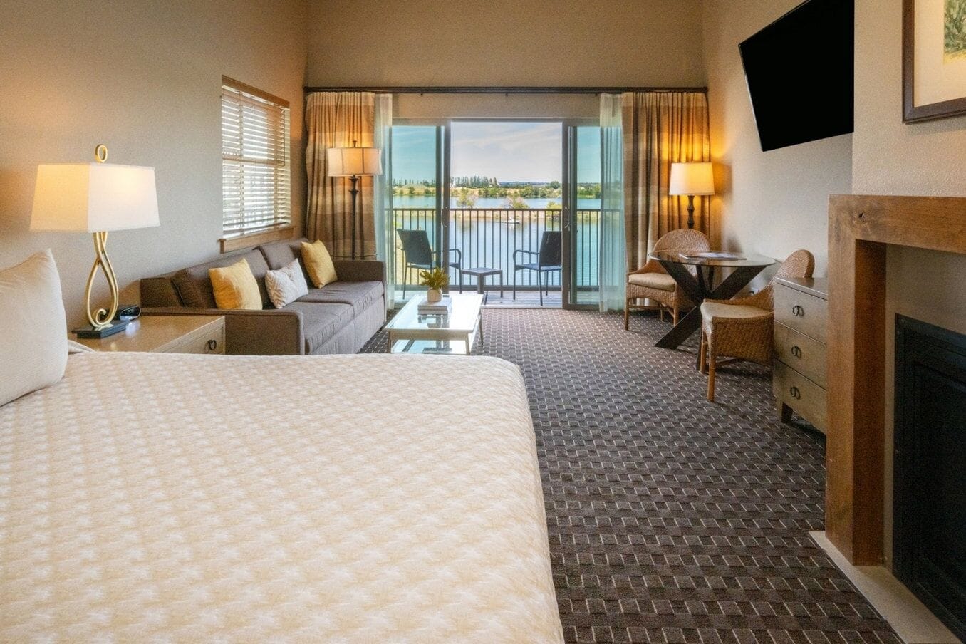 Une chambre d’hôtel avec un grand lit, un canapé, une petite table, une chaise, une cheminée et un balcon avec vue.