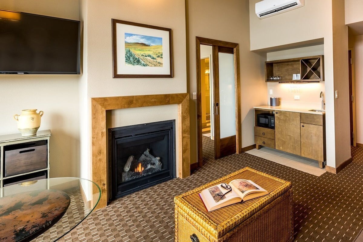 Una habitación de hotel con chimenea, televisión, zona de cocina y mesa de comedor.