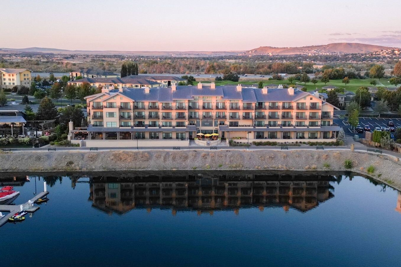 Un hôtel à plusieurs étages avec une piscine dont la surface réfléchit la lumière, située à l’avant.