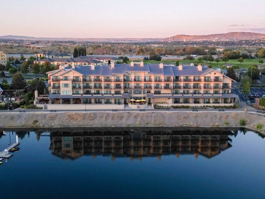 Un hôtel à plusieurs étages avec une piscine dont la surface réfléchit la lumière, située à l’avant.