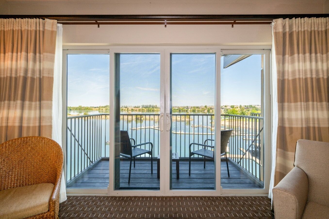 A balcony with two chairs and a wicker chair, overlooking a body of water with a distant landscape.