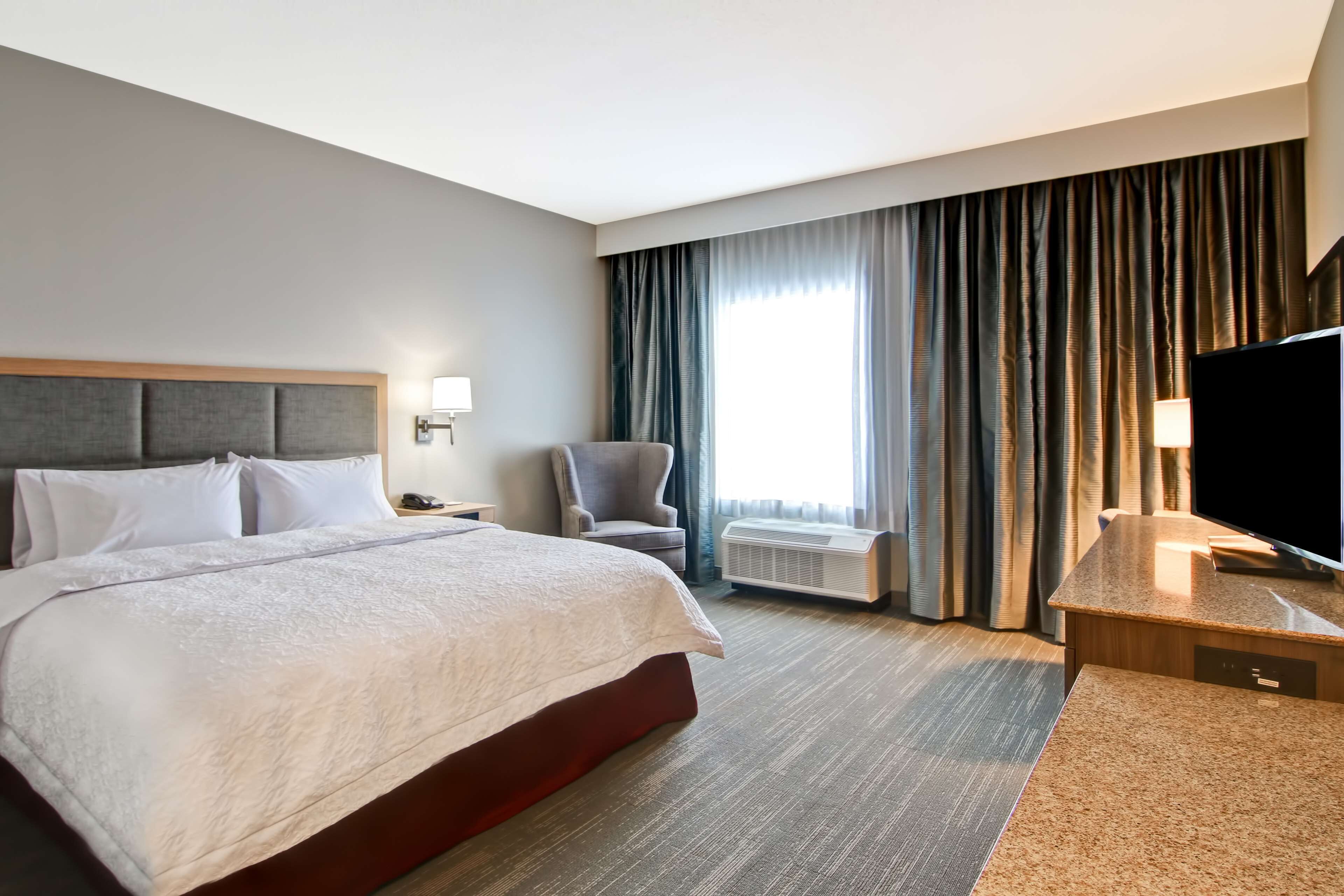 A hotel room with a large bed, a desk with a flat-screen TV, a chair, and a window with curtains.