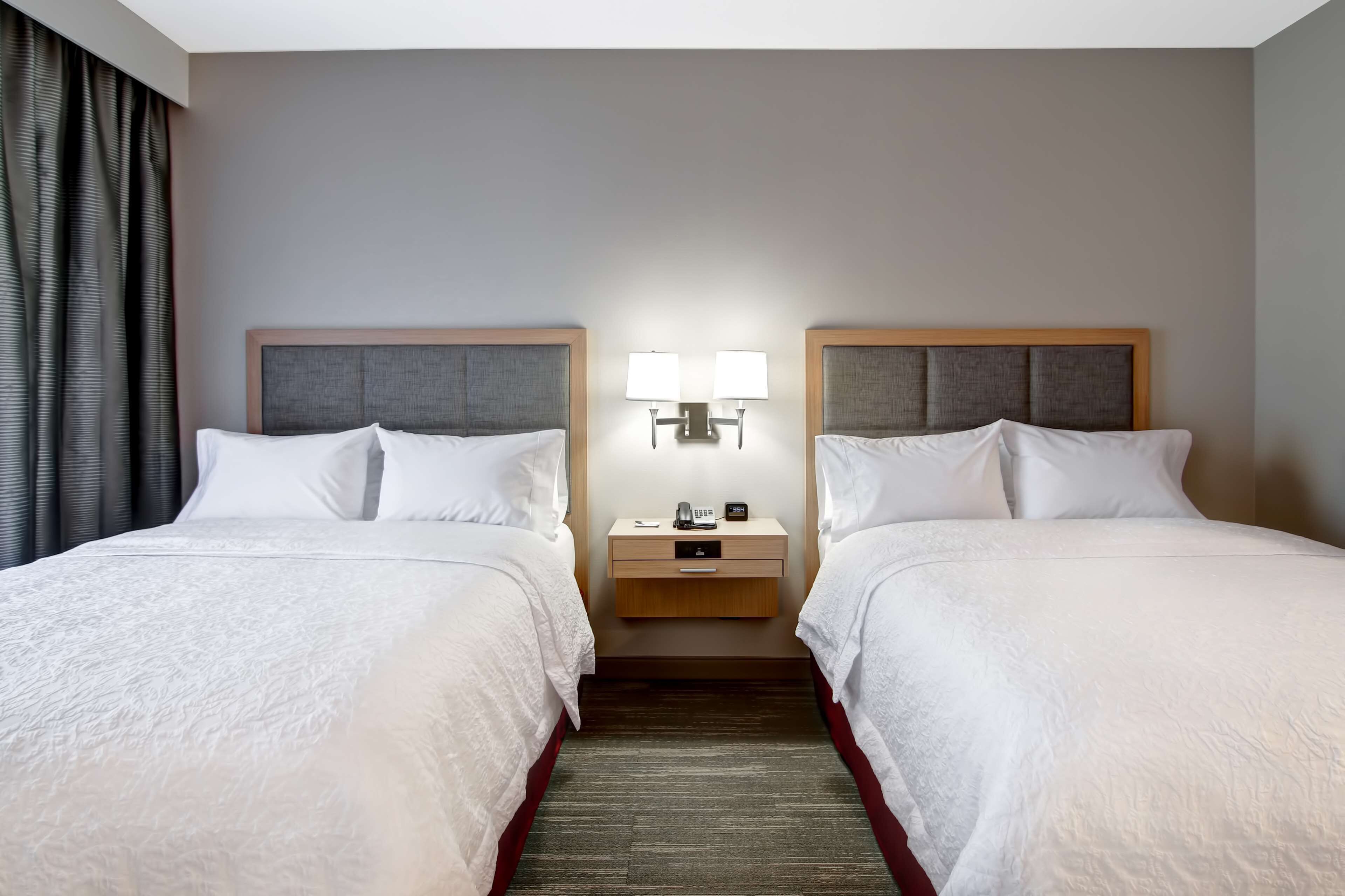 A hotel room with two beds, a nightstand with lamps, and a wooden headboard.