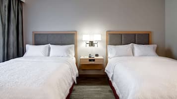 A hotel room with two beds, a nightstand with lamps, and a wooden headboard.