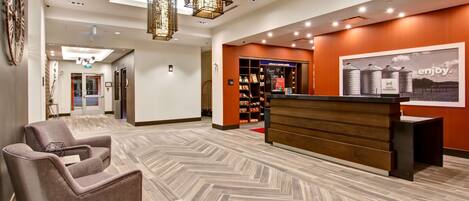 A hotel lobby with a reception desk, a seating area, and a wall with a poster.