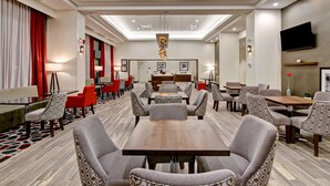 A hotel lobby with a central seating area, multiple tables, and chairs.