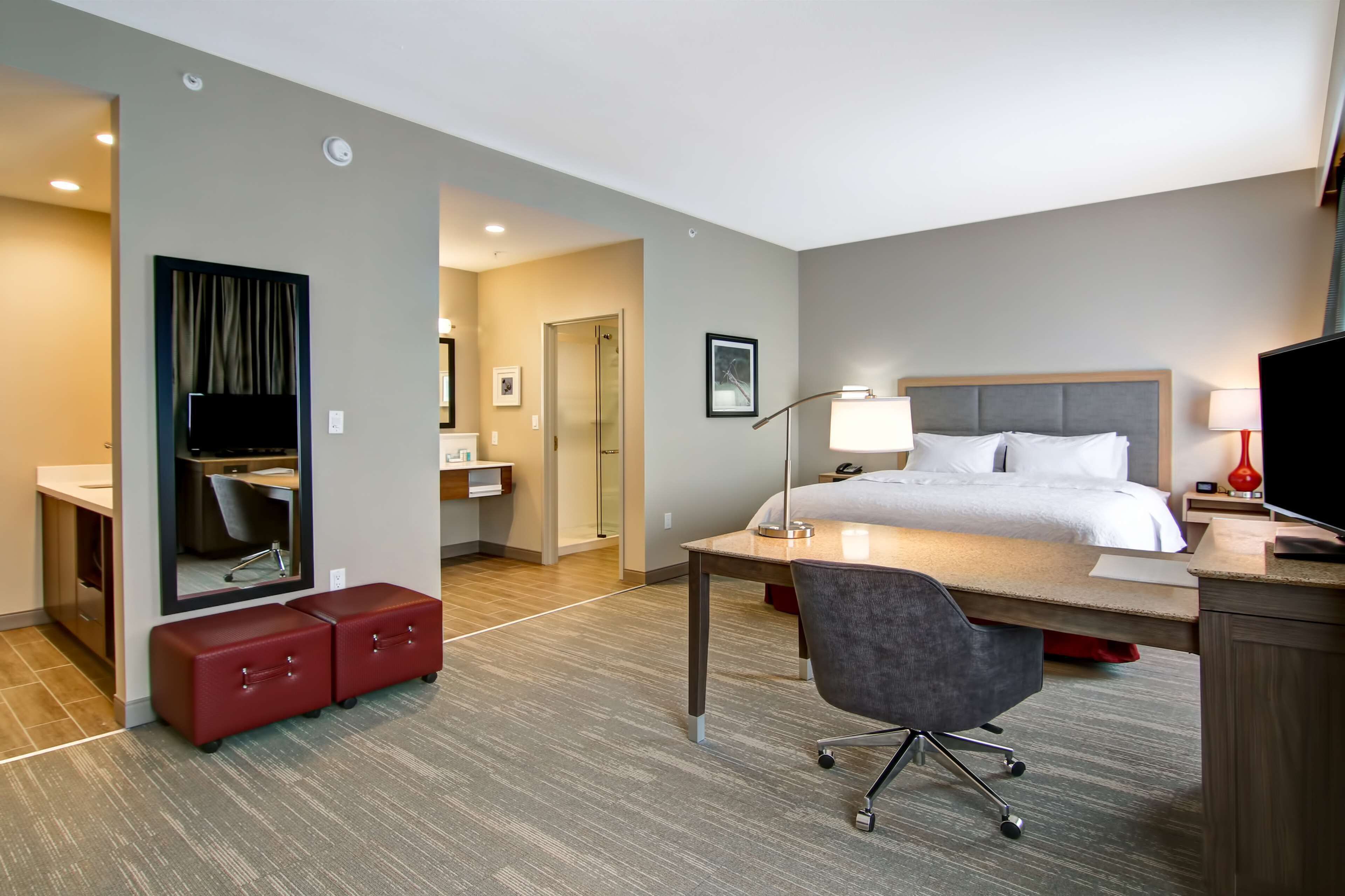 A hotel room with a bed, desk, chair, and a mirror.