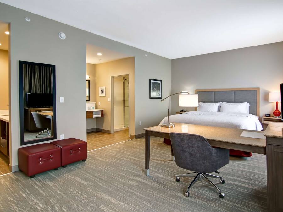A hotel room with a bed, desk, chair, and a mirror.