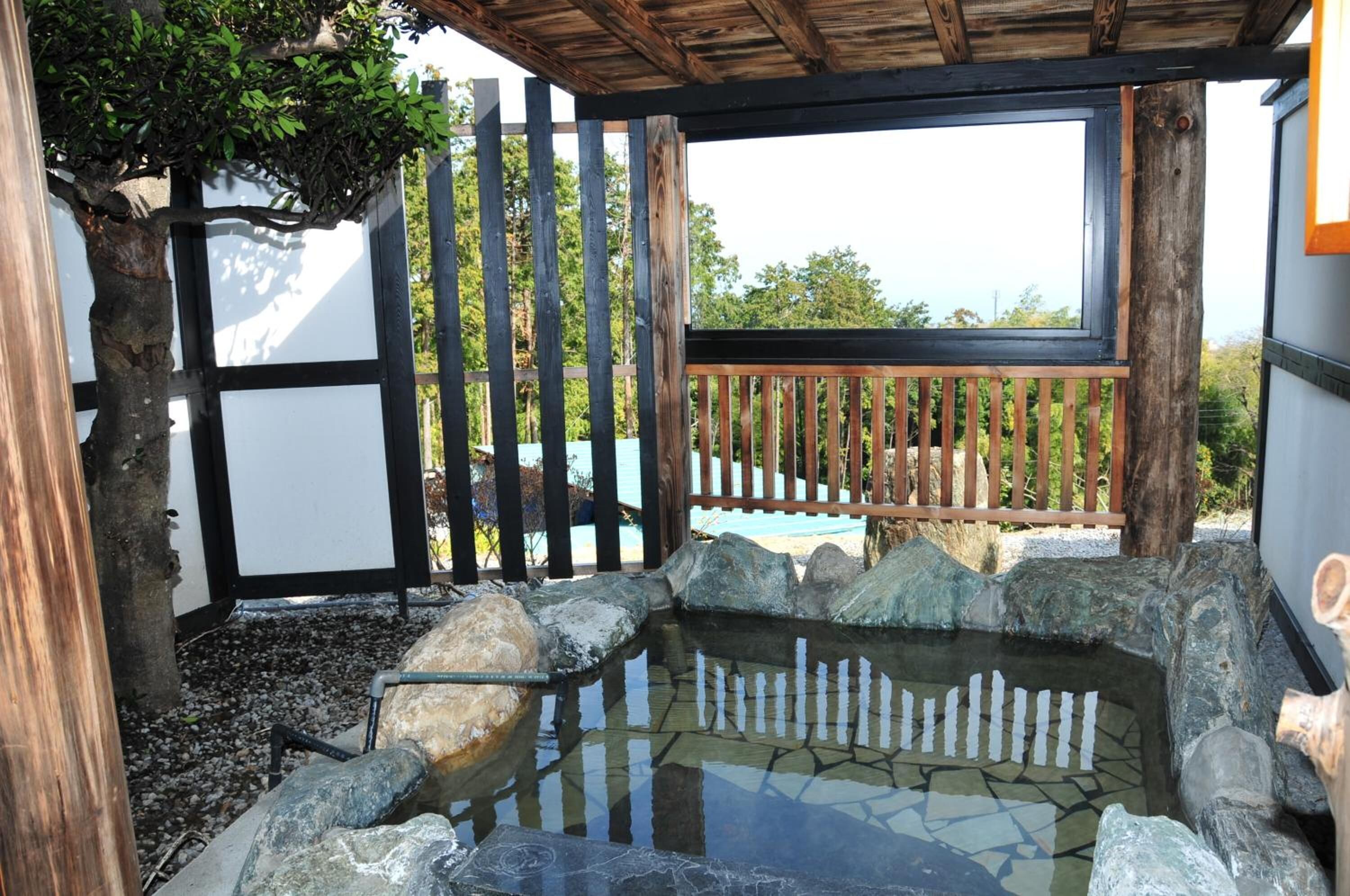 Un jardín japonés tradicional con un estanque de piedra, valla de madera y vistas a una playa.