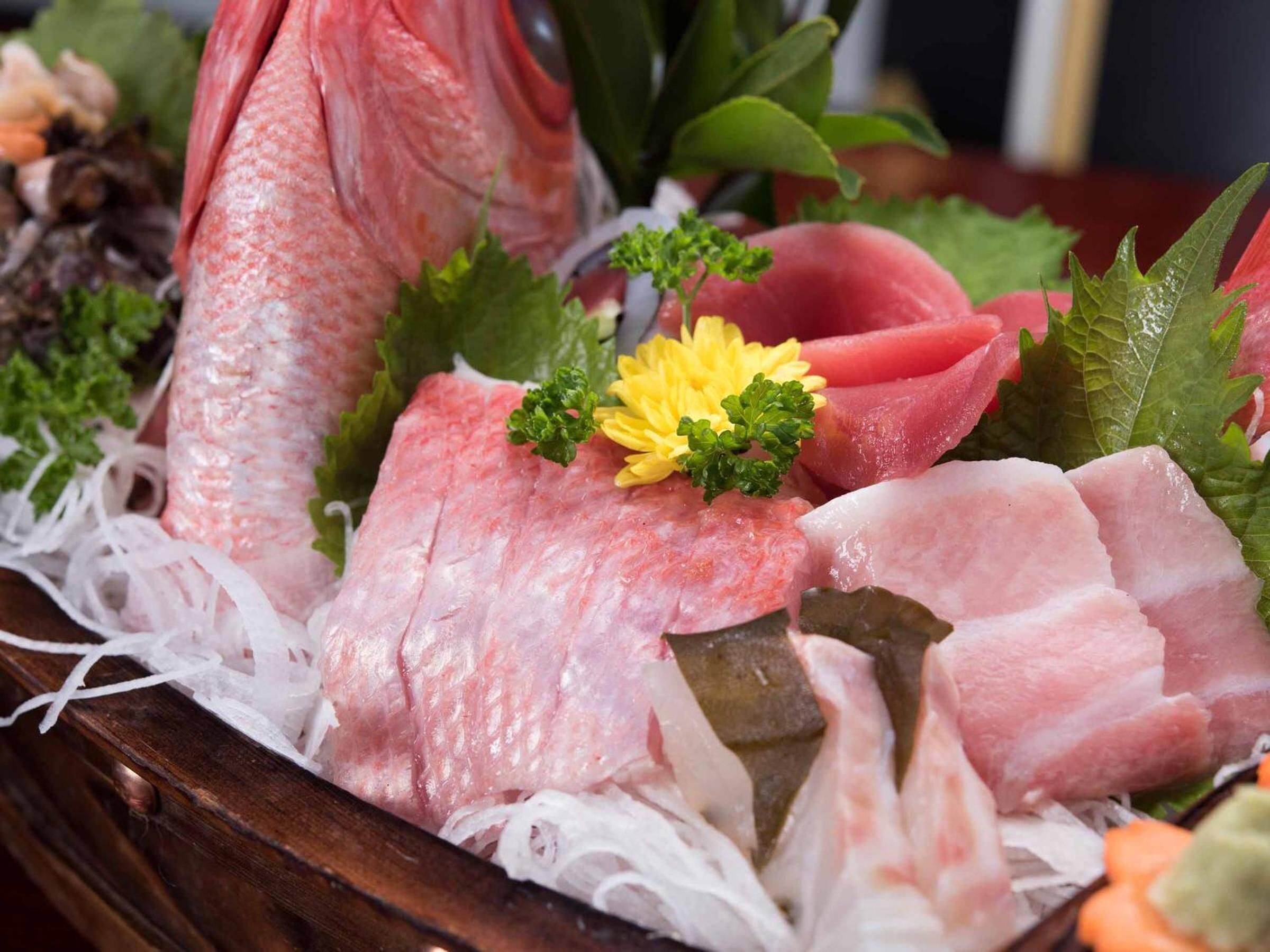 Fisk og skaldyr i frisk kvalitet, anrettet på en træoverflade med dekorative elementer som blomster og blade.
