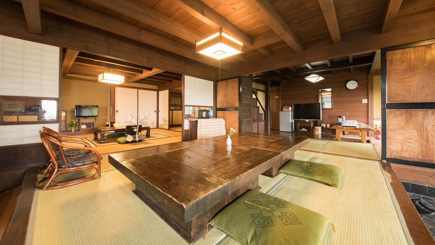 Una habitación tradicional japonesa con suelo de tatami, una mesa de madera baja, un banco de tatami, un televisor y una puerta corredera.
