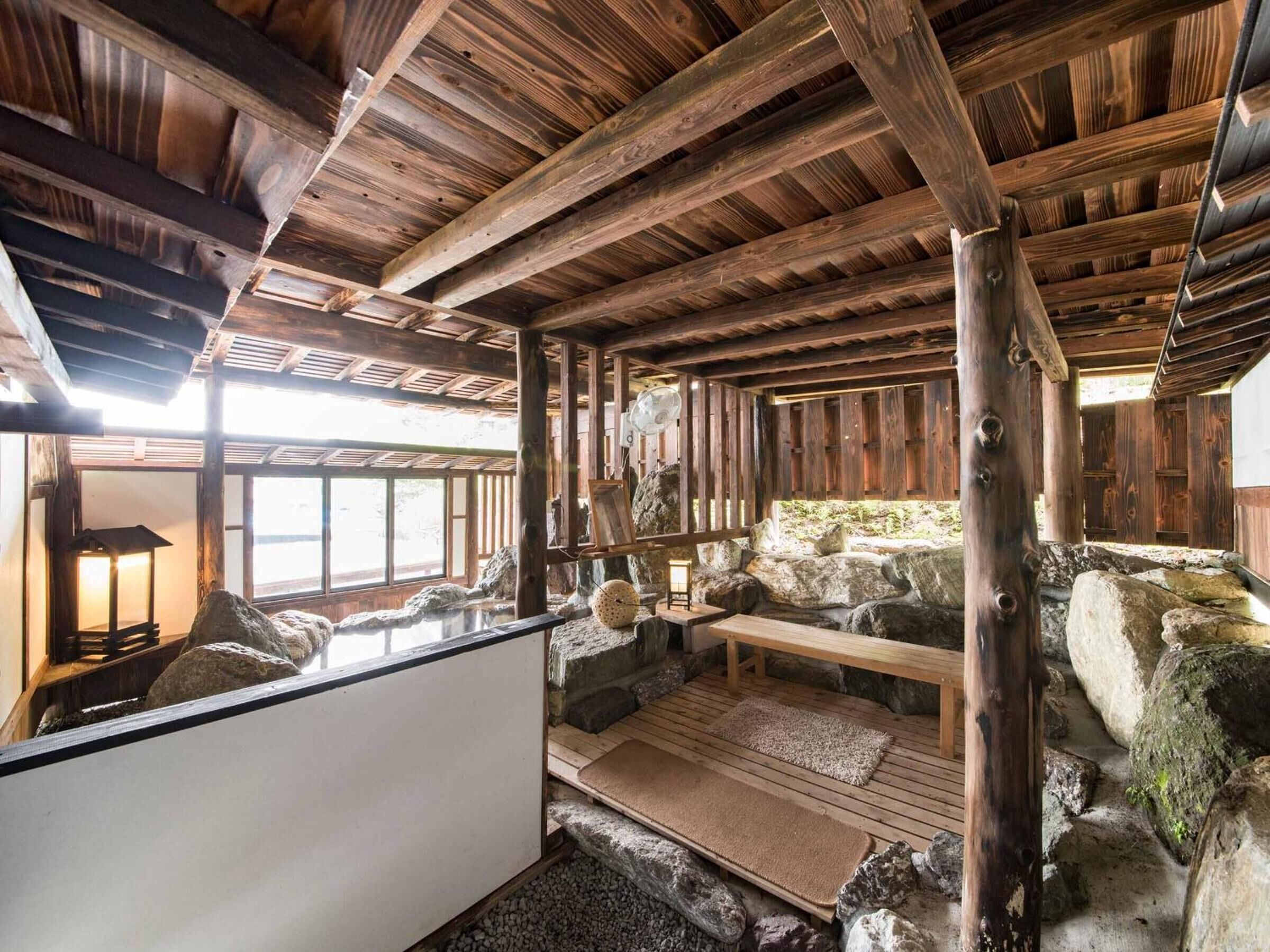 A rustic interior with wooden beams, a stone fireplace, and a seating area with a bench and cushions.