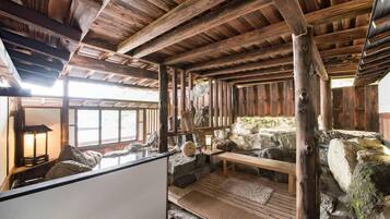 A rustic interior with wooden beams, a stone fireplace, and a seating area with a bench and cushions.