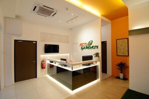 A reception desk with a sign reading "Eco Garden," a fire extinguisher, a flat-screen TV, and a potted plant. - Eco Garden Hotel (Serendah)
