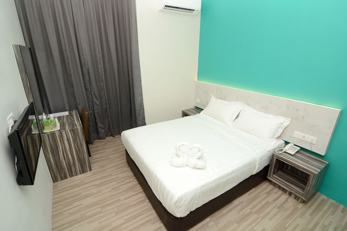 Una habitación de hotel con cama, mesita de noche con teléfono, espejo y escritorio con computadora y una botella.