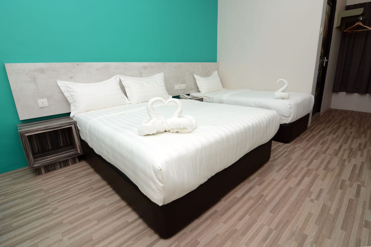 Habitación de hotel con dos camas, cada una con ropa blanca y una toalla con forma de cisne. El suelo es de madera y la pared es de color aguamarina.