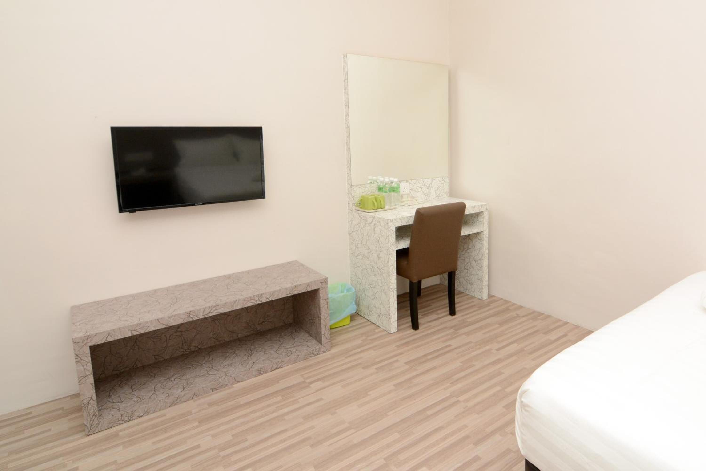 A hotel room with a bed, a desk with a chair, a TV mounted on the wall, and a bench.