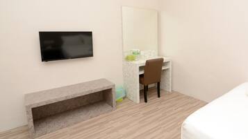 A hotel room with a bed, a desk with a chair, a TV mounted on the wall, and a bench.