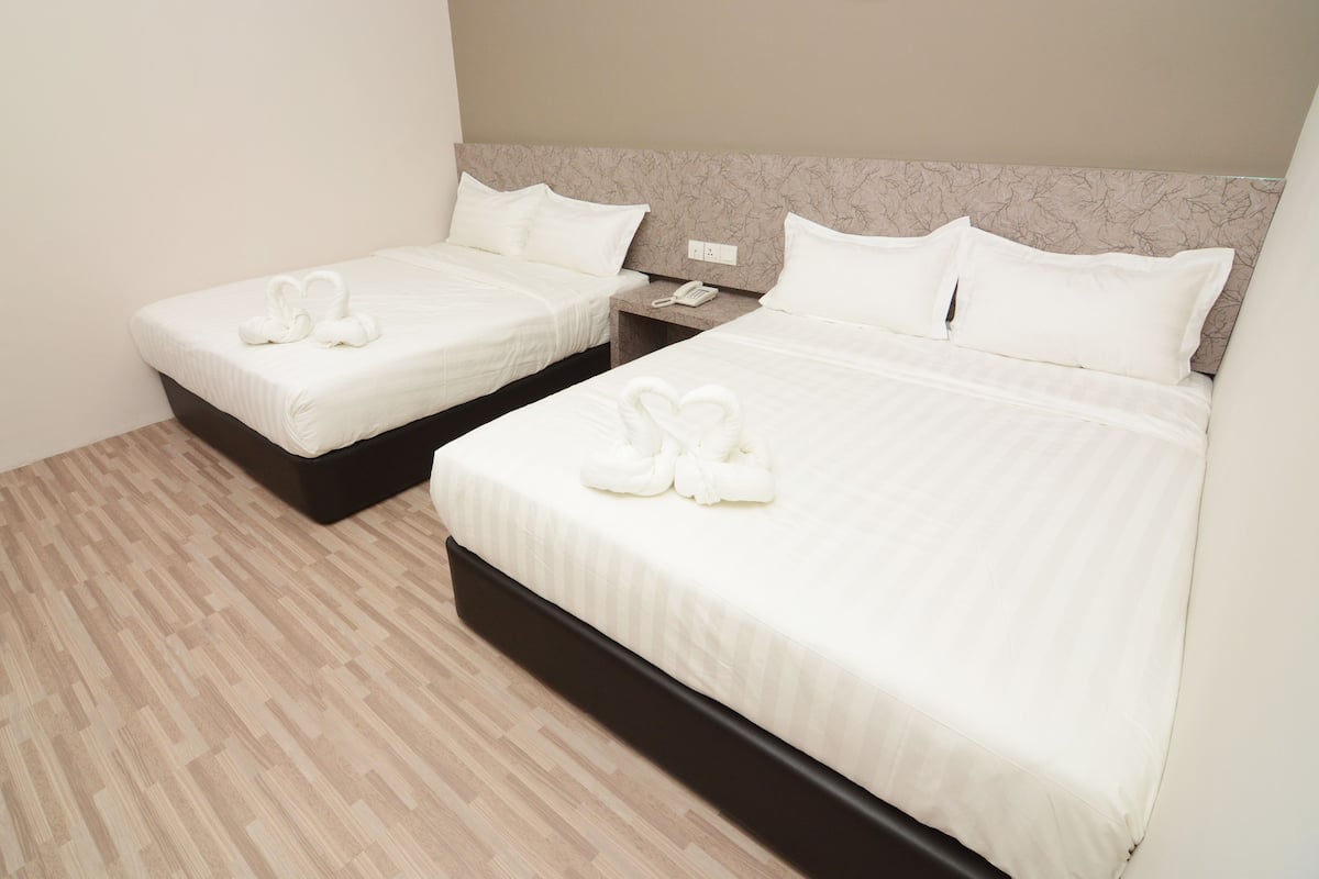 Dos camas individuales con sábanas y toallas blancas, un teléfono junto a la cama y suelo de madera.