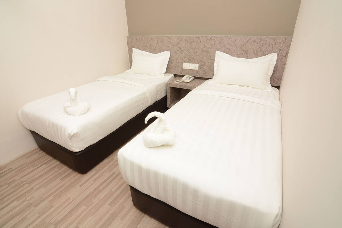 Dos camas individuales con sábanas blancas y toallas con forma de cisne, un teléfono junto a la cama y un cabecero con estampado de mármol.
