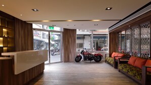 A reception area with a wooden reception desk, a motorcycle, and seating with orange cushions. - Home Rest Hotel (Taitung)