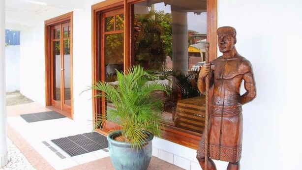 Une entrée d’immeuble avec des portes en bois, une plante en pot et une statue en bois.