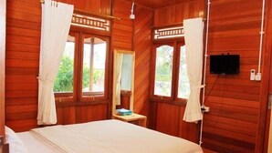 Ein Zimmer mit Holzboden, einem Bett, Vorhängen, einem Fernseher und einem kleinen Tisch.