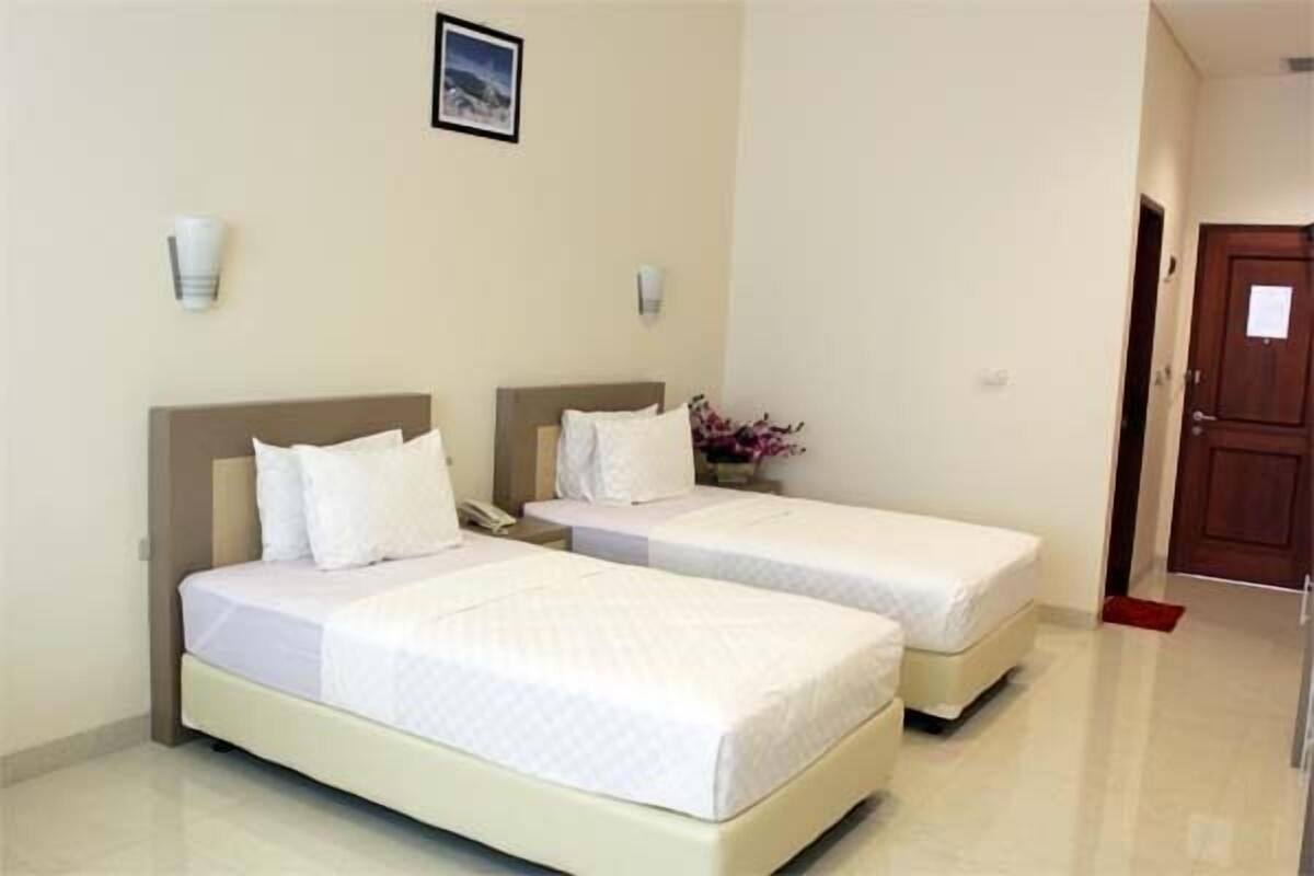 A hotel room with two single beds, a nightstand, a telephone, and a small table with a vase of flowers.