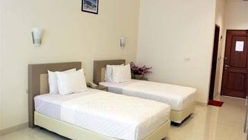 A hotel room with two single beds, a nightstand, a telephone, and a small table with a vase of flowers.