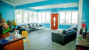 A living room with a sofa set, a coffee table, a yellow chair, and a desk with a vase of flowers. - Ulalei Lodge (Apia)