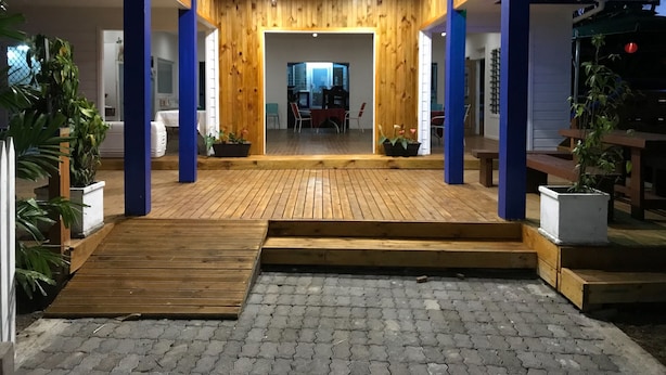 A wooden entrance with a ramp leading to a covered area, surrounded by potted plants and a seating area. - Ulalei Lodge (Apia)