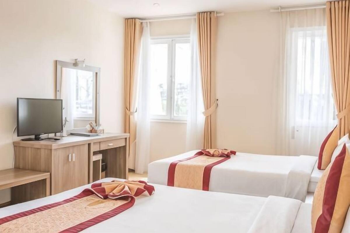 Habitación de hotel con dos camas, un escritorio con televisor y ventanas grandes con cortinas.