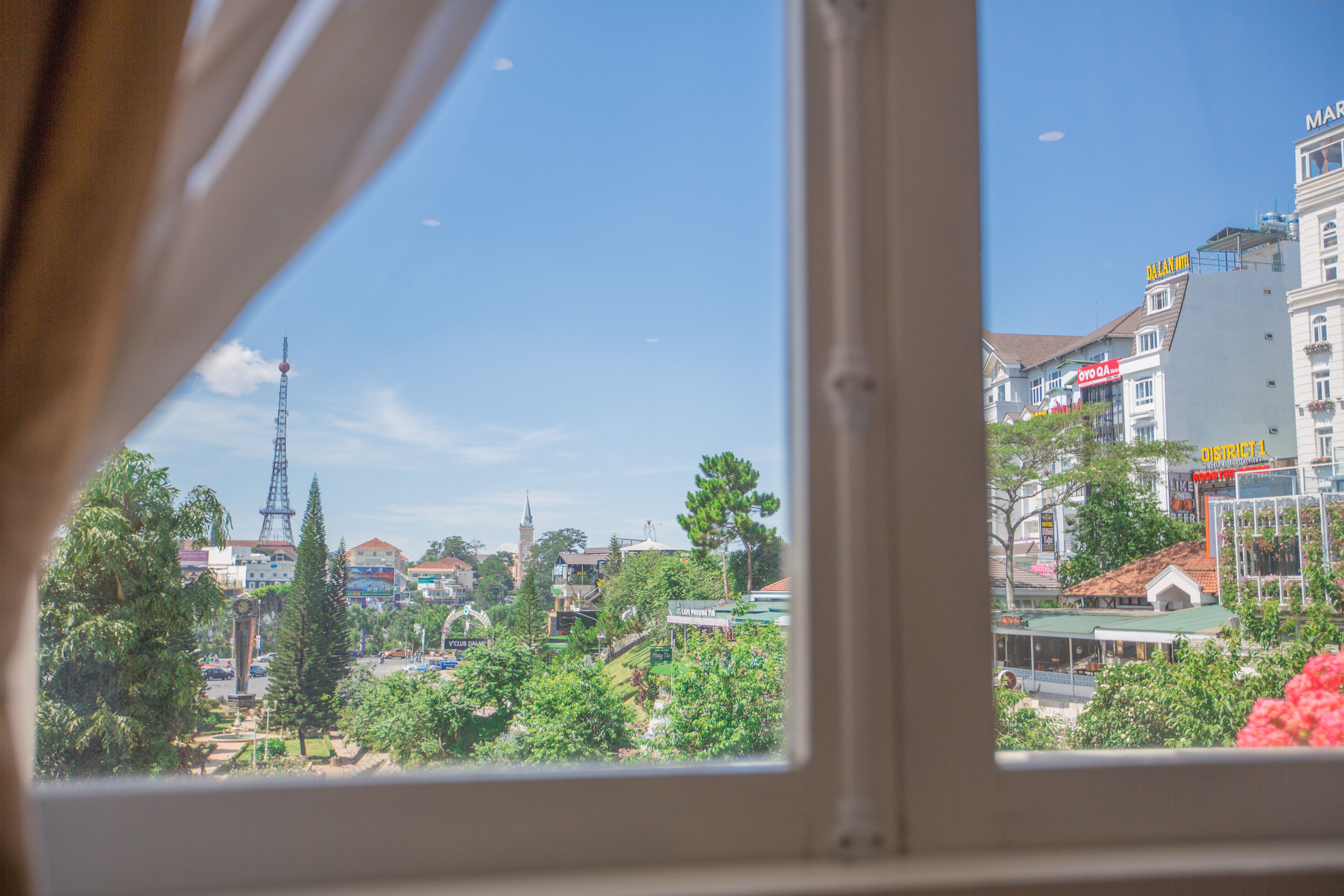 A view through a window of a cityscape with buildings, a tower, and greenery.