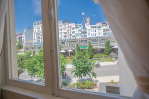 A view of a hotel with multiple floors and balconies, a street with trees and a few people, and a clear blue sky. - Nice Dream Dalat Hotel (Xuan Huong - Da Lat)