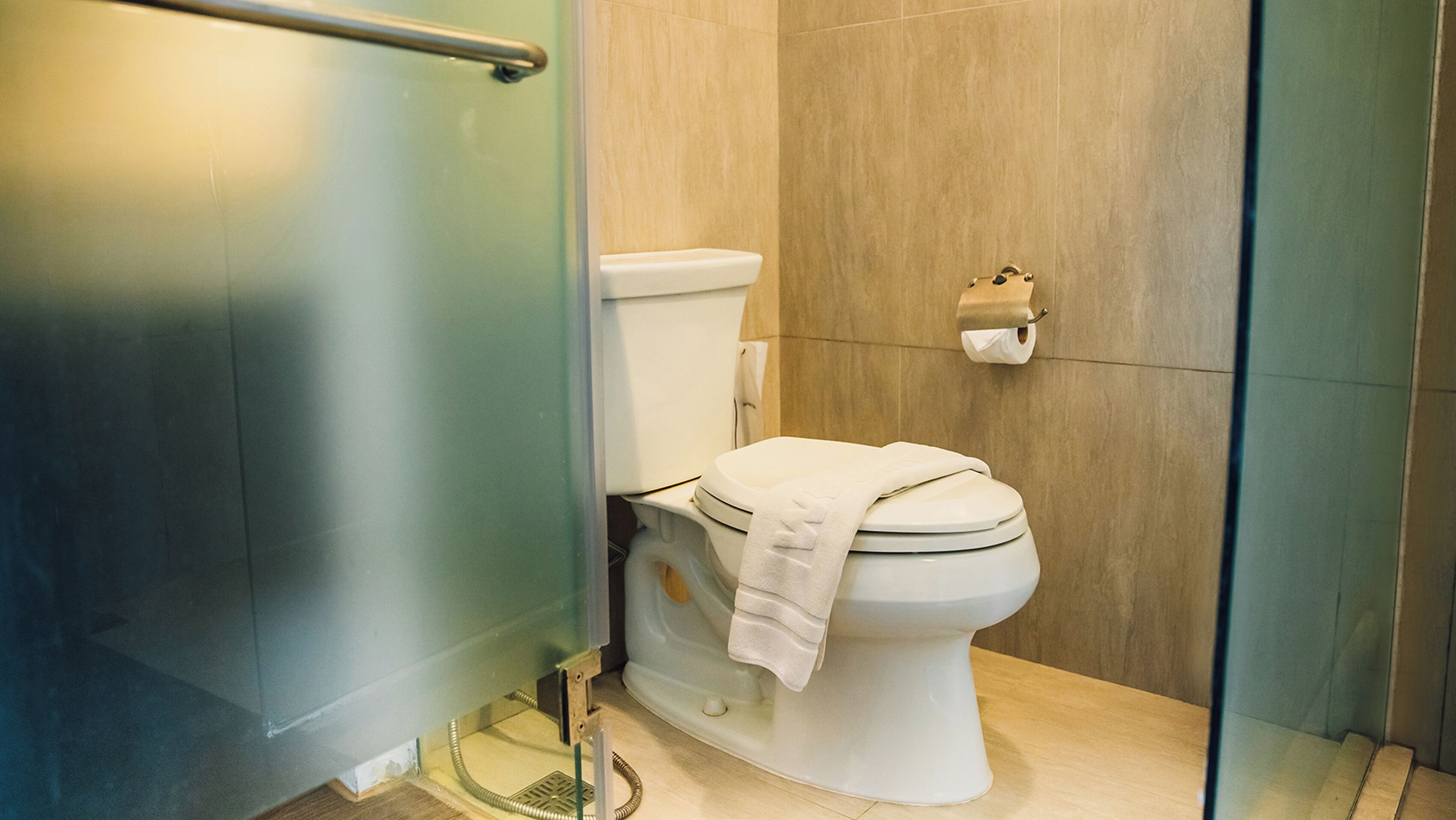 A modern bathroom with a toilet, a towel on the seat, and a toilet paper holder on the wall.
