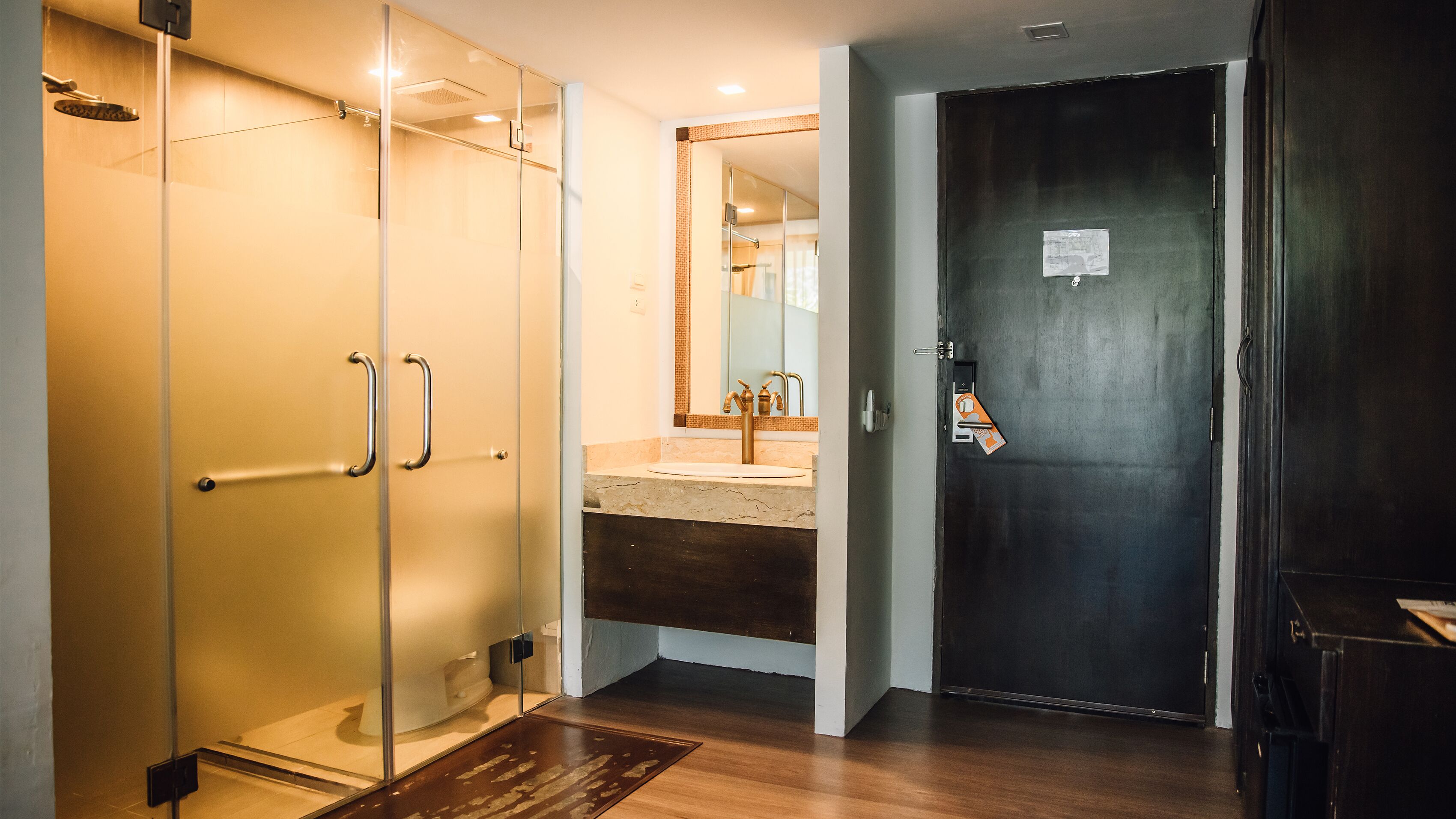 A modern bathroom with a glass shower enclosure, a sink with a mirror, and a dark door.