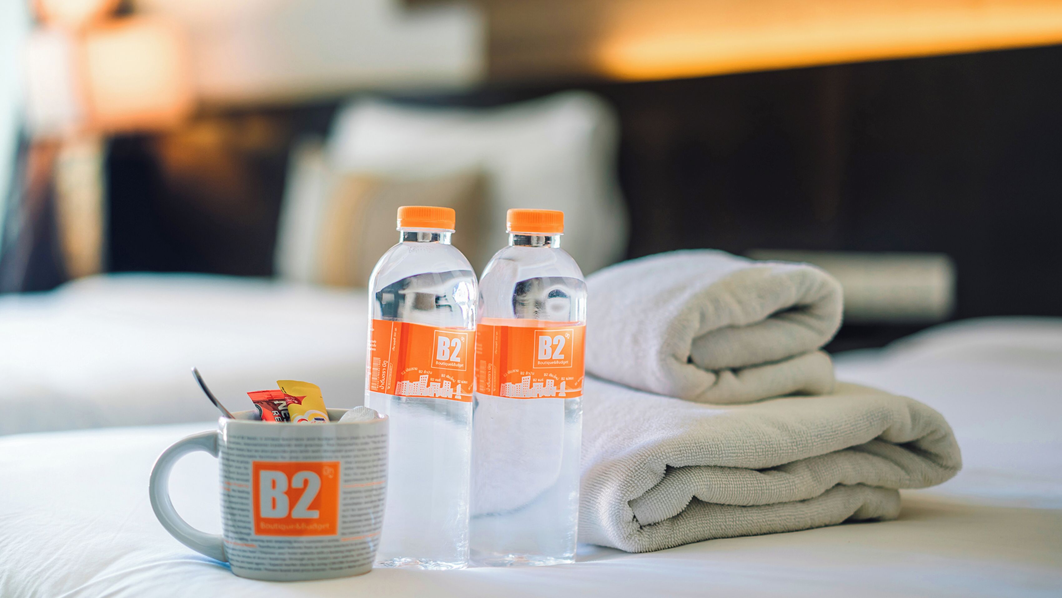 A neatly made bed with two bottles of water, a mug, and a folded towel.
